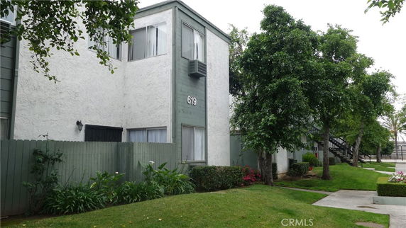 Front view of a two-story apartment building with a green fence and surrounding trees.