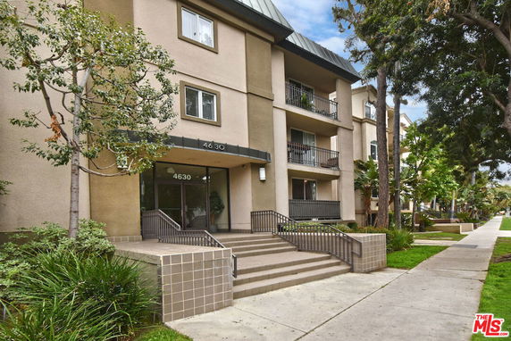 Front view of a three-story apartment building with balconies and an entrance with stairs.