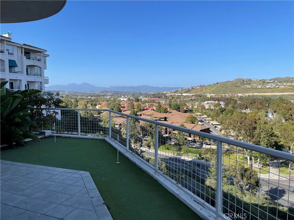 View from a balcony overlooking buildings and a vast landscape with hills in the distance.