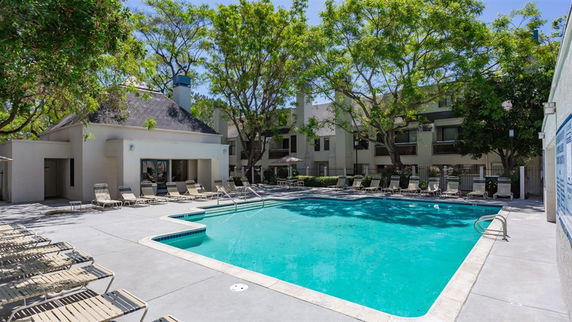 Outdoor swimming pool with lounge chairs surrounding it, adjacent to residential buildings.