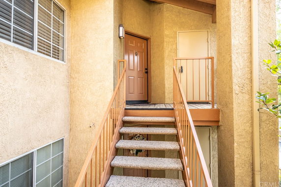 Front view of an apartment building entry with stairs leading to a brown door.
