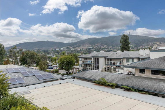 Rooftop with solar panels and view of nearby buildings and mountains.