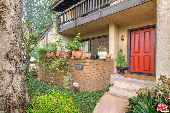Front view of a house with a red door and balcony, surrounded by plants.
