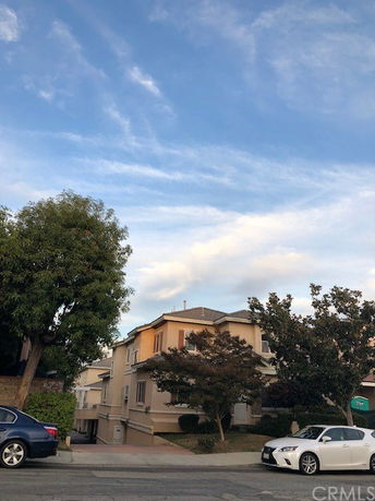 Front view of a multi-story residential building with trees and parked cars.