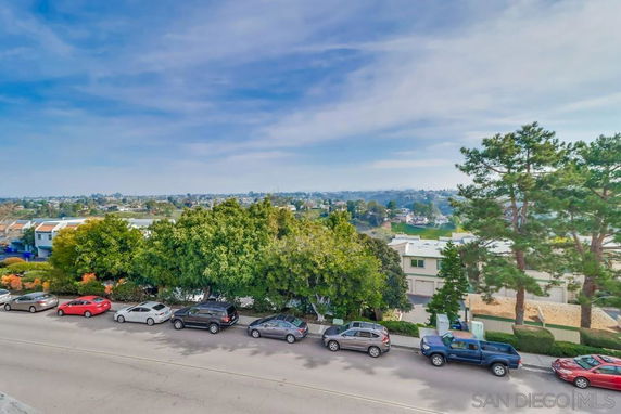 View of a suburban neighborhood with trees and parked cars along the street.