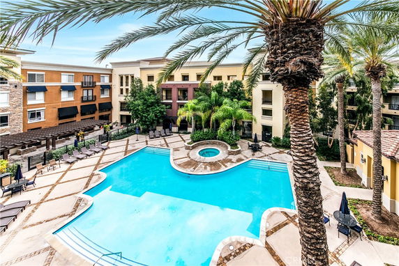 Outdoor view of a swimming pool area surrounded by apartment buildings and palm trees.