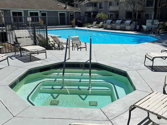 Outdoor swimming pool area with surrounding seating and a hot tub.