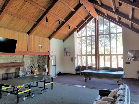 Interior view of a clubhouse with a high wooden ceiling, large windows, a fireplace, and recreational tables.