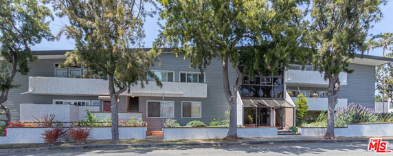 Front view of a two-story building with balconies and trees in front.