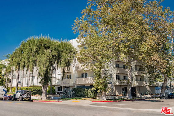 Front view of a multi-story building with balconies and large trees in front.