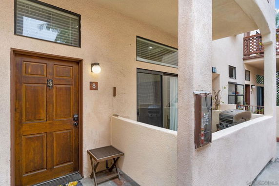 Front view of a multi-level building entryway with a wooden door and a small patio area.