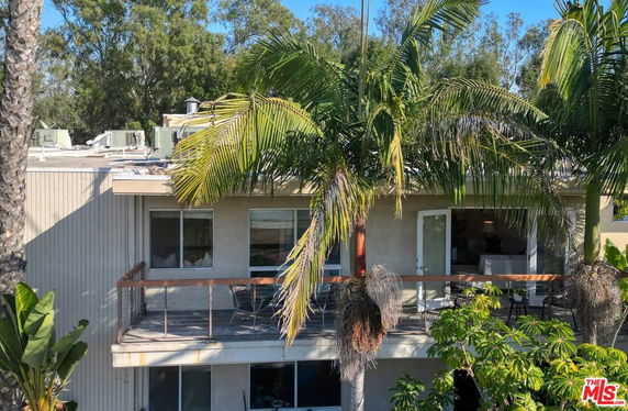 Front view of a multi-story house with a balcony and surrounding trees.