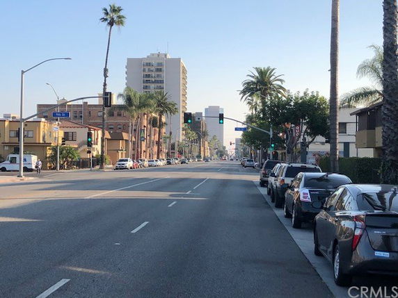 Street view of urban area with buildings and parked cars along the road.
