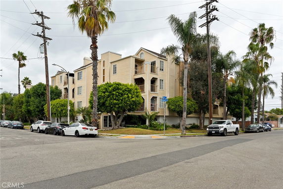 Front view of a multi-story apartment building with balconies, surrounded by palm trees.