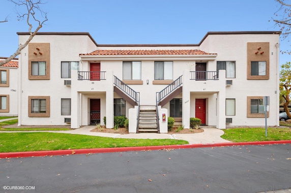 Front view of a two-story apartment building with external staircases and red doors.