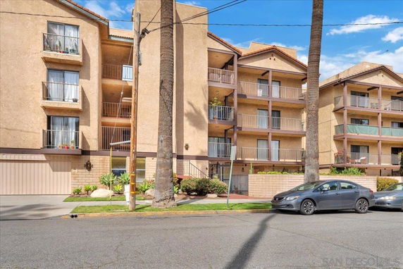 Front view of a multi-story apartment building with balconies and parking area.