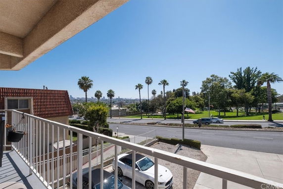 Balcony view overlooking a street with palm trees and a park area.