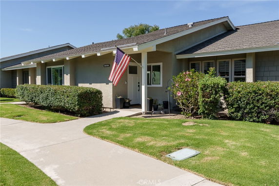 Front view of a single-story house with an American flag and manicured shrubs.