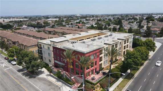 Aerial view of a multi-story apartment building with a red and beige facade, surrounded by streets and neighboring residential areas.