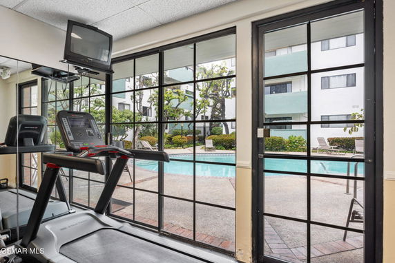 Indoor gym area with treadmills facing large windows overlooking a swimming pool.