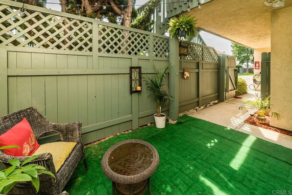 Outdoor patio area with green fencing and sitting area with chairs and table.