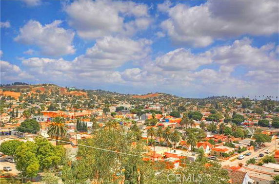 A wide view of a suburban area with houses, trees, and hills in the background under a partly cloudy sky.