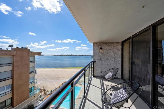 Balcony with chairs overlooking a sandy beach and water.