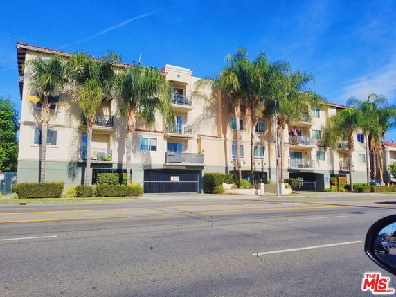 Front view of a multi-story apartment building with balconies and palm trees.