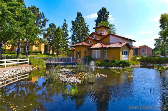 View of a yellow house with a red-tiled roof near a pond, surrounded by trees.