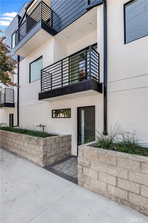 Front view of a modern multi-story building with balconies and a small entrance courtyard.
