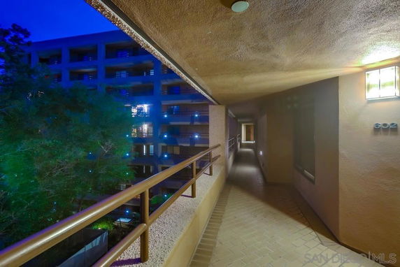Exterior corridor with railing overlooking a multi-story building and trees at night.