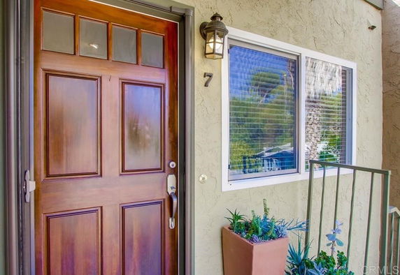 Front view of an entrance door with a window and potted plants.