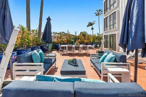 Outdoor seating area with sofas, tables, and umbrellas on a tiled patio.