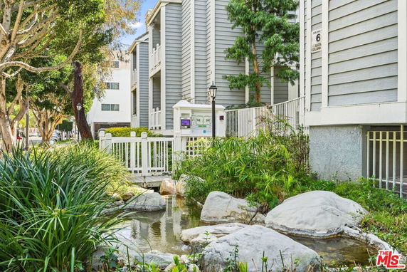 Front view of a multi-story building with a gray exterior and a small garden with a water feature.