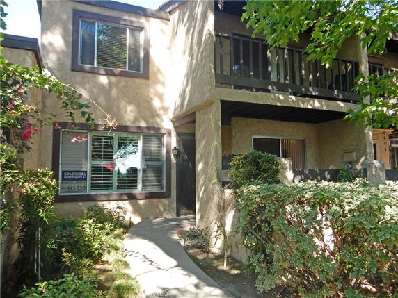 Front view of a two-story house with a balcony and surrounding plants.
