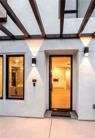 Front view of a modern house entrance with wooden beams and illuminated wall lights.