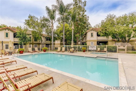Outdoor swimming pool area with sun loungers and fenced surroundings.
