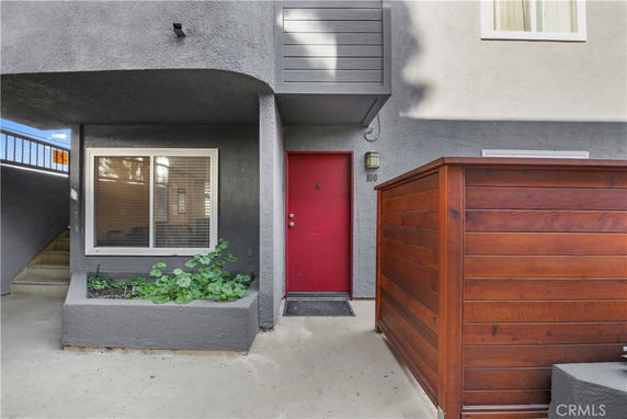 Front view of a building entrance with a red door and a wooden privacy fence.