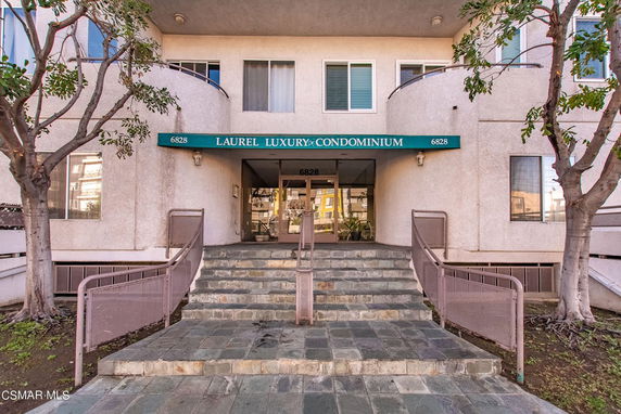 Front view of a condominium building entrance with stairs and canopy.