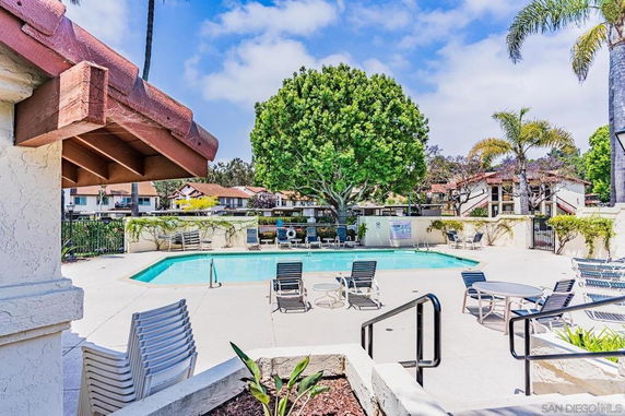 Outdoor swimming pool with surrounding deck chairs and a tree in a residential area.