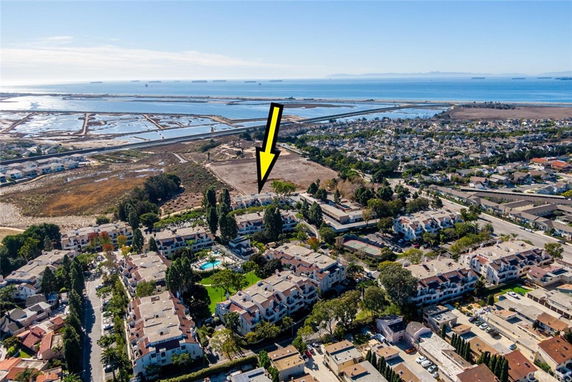 Aerial view of a coastal residential area with houses, roads, and water bodies in the background.