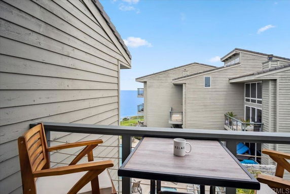 View from a balcony with a table and chairs overlooking the ocean and neighboring buildings.