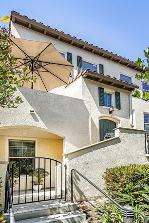 Front view of a multi-story house with balcony and patio umbrella.