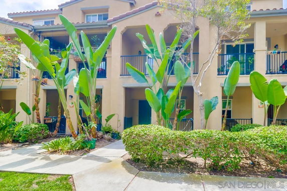 Front view of a multi-story residential building with balconies and lush greenery.