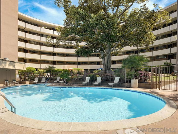 Outdoor swimming pool in front of a multi-story apartment building with curved balconies.