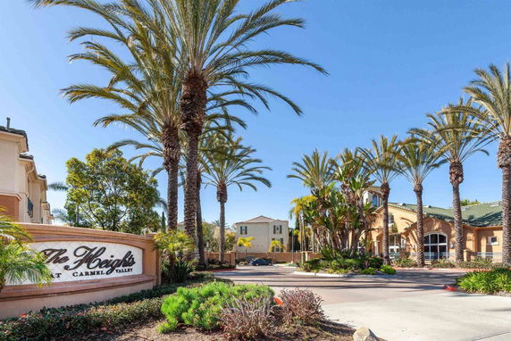 Front view of a residential complex entrance with palm trees and signage.