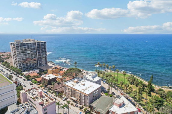 Aerial view of buildings near the ocean with clear blue water and a green park.
