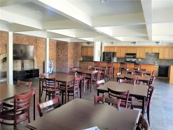 Common area with tables and chairs, a TV, and a kitchen in the background.