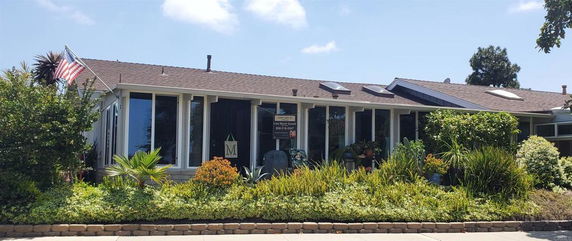 Front view of a single-story house with large windows, solar panels, and a neatly landscaped garden.