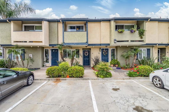 Front view of a two-story townhouse with decorative balconies and surrounding greenery.